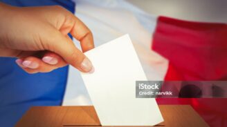 Hand putting a voting ballot into box and French flag on the background