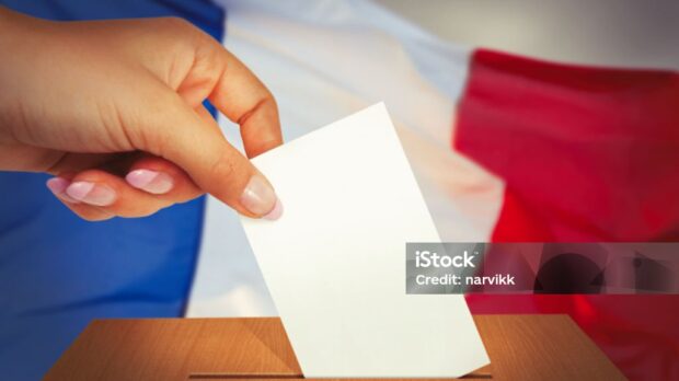 Hand putting a voting ballot into box and French flag on the background